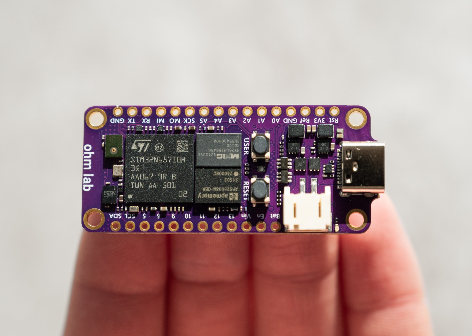 Neuro N6 STM32N6 board held on a fingertip, showing its compact size and labelled Feather pinout